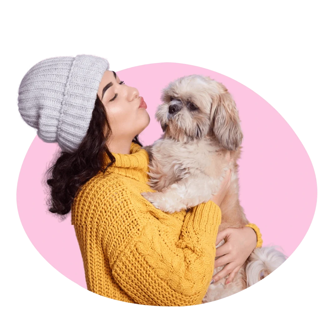 Smiling woman in yellow sweater holding and kissing her fluffy dog – About Heart N Paws